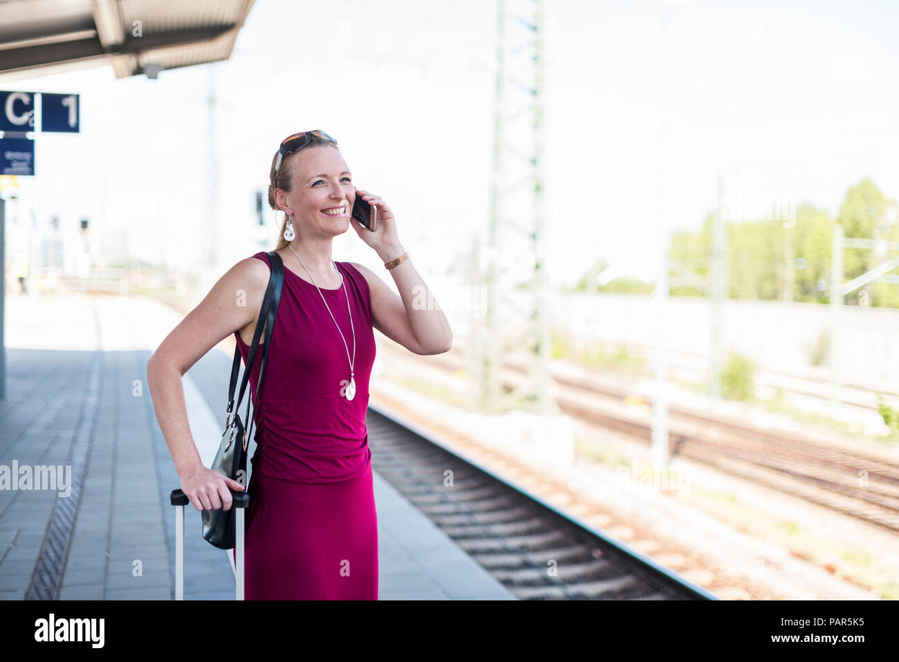 Smiling mature woman on the phone waiting at platform Stock Photo