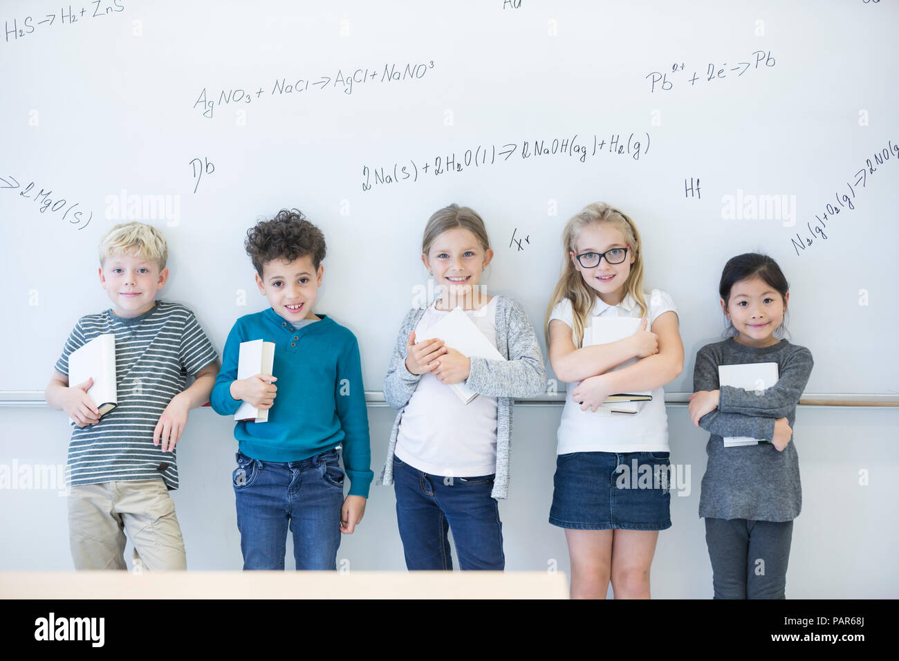 Portrait of smiling pupils standing at whiteboard with formulas in class Stock Photo