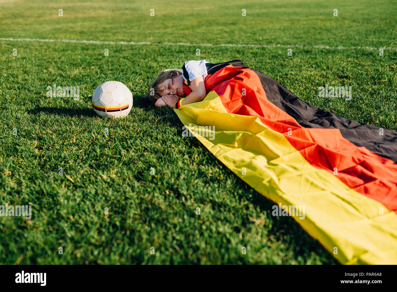 Boy sleeping on soccer field, covered iwith German flag Stock Photo