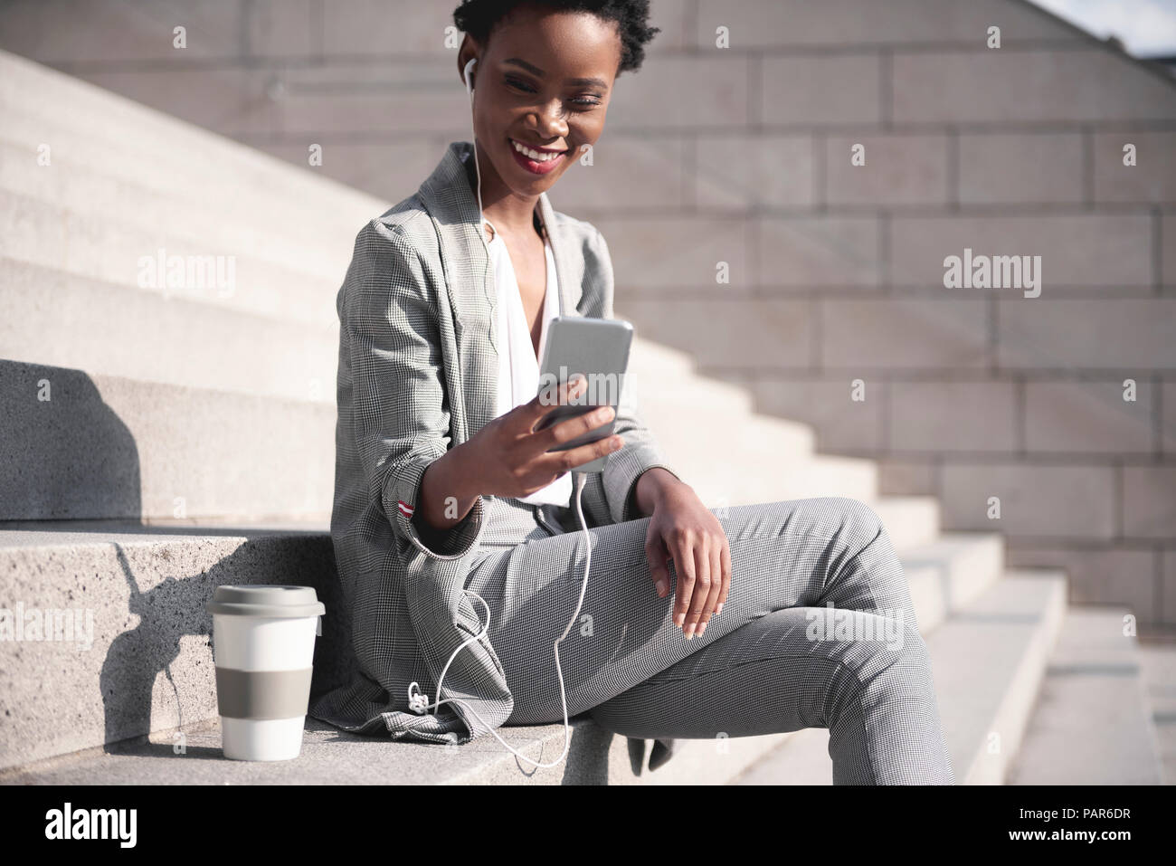 Portrait of smiling businesswoman sitting on stairs using earphones and smartphone Stock Photo