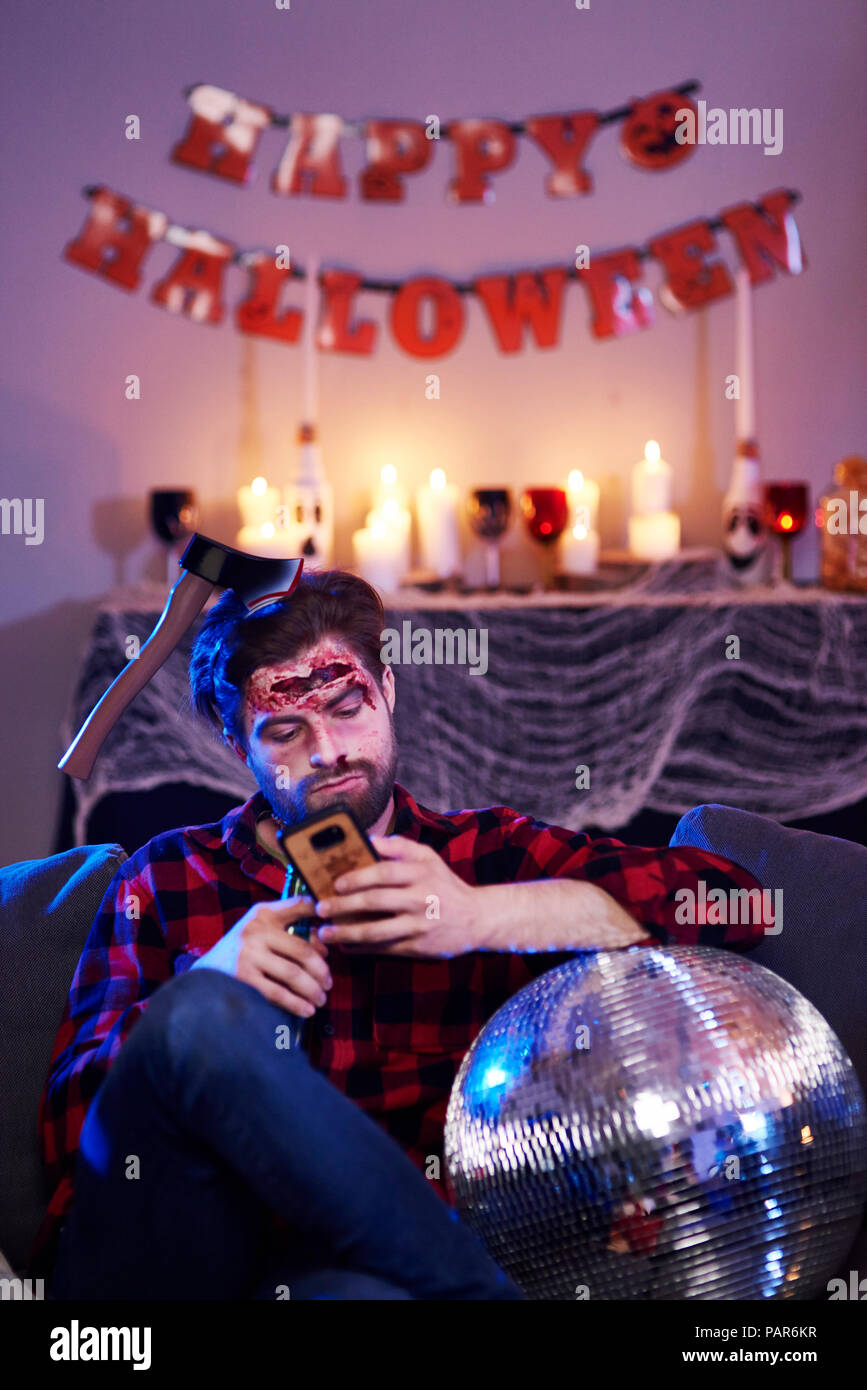 Bored man using mobile phone at Halloween party Stock Photo