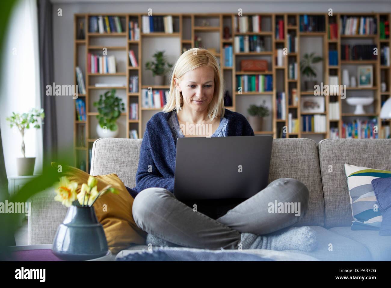 Woman at home sitting on couch using laptop Stock Photo