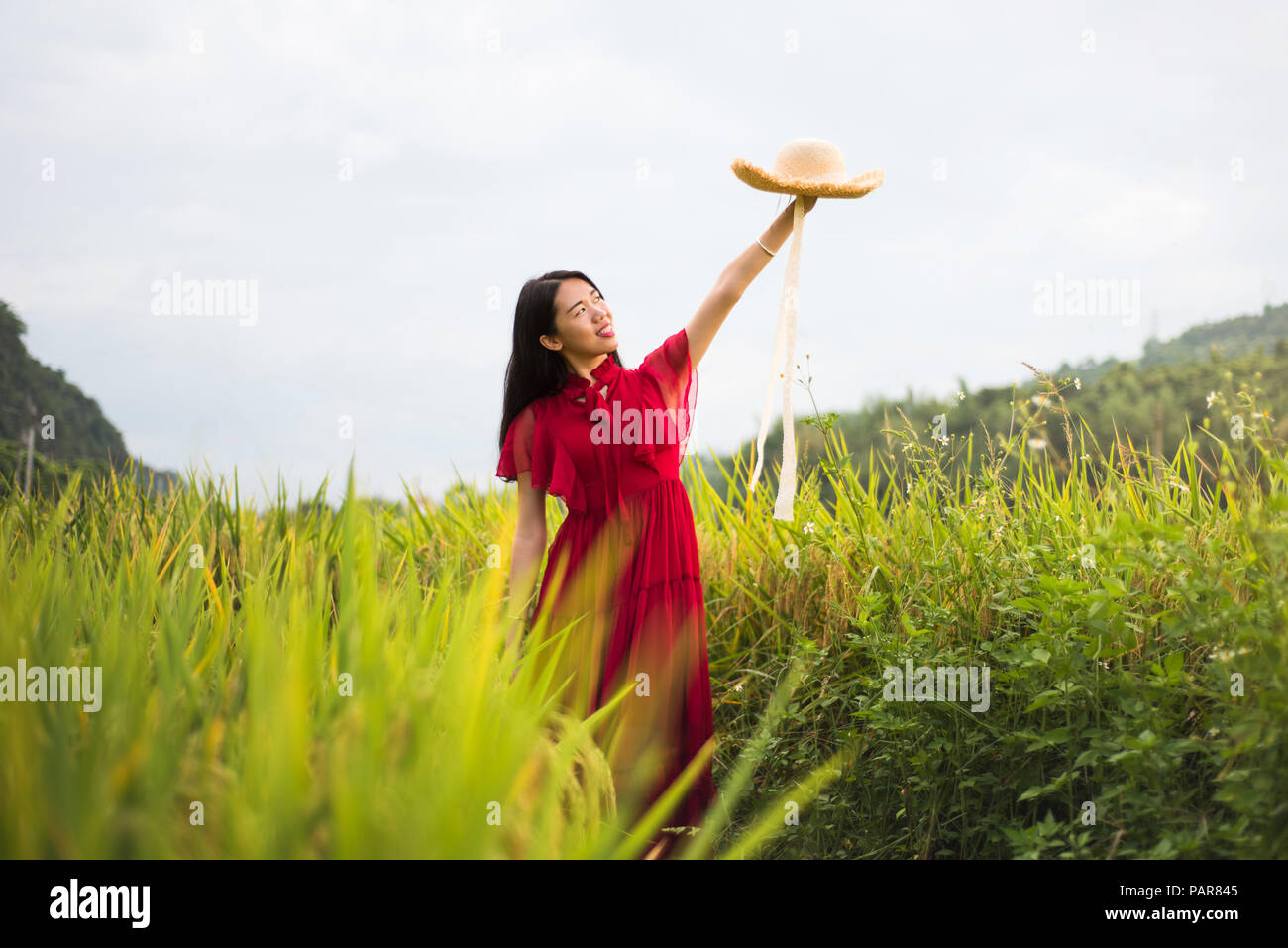 Girl in a rice field wearing red dress and a hat Stock Photo