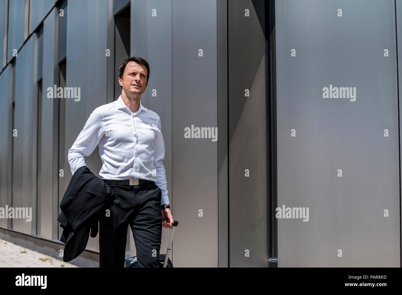 Businessman with rolling suitcase walking in the city Stock Photo