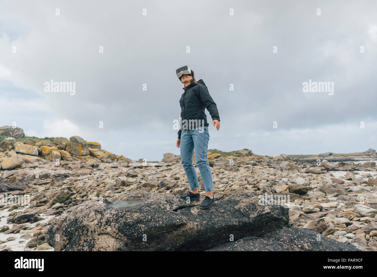 France, Brittany, Landeda, young woman standing at the coast wearing VR glasses Stock Photo