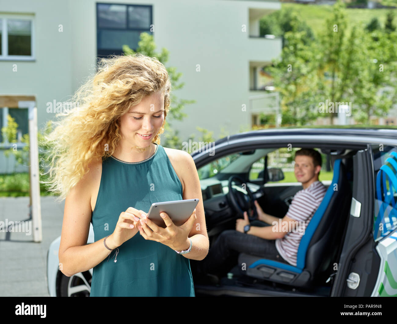 Smiling young woman using tablet with man sitting in electric car in background Stock Photo