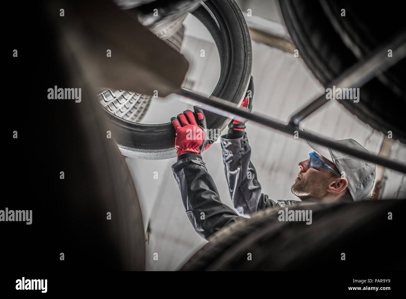 Vulcanizing Services Worker. Tires and Alloy Wheels Sales. Caucasian Vulcanization Technician Removing Tire From the Storage Shelf. Stock Photo