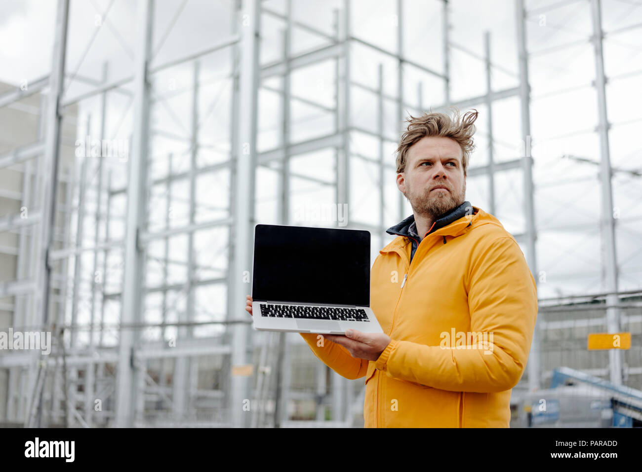 Man holding laptop, construction site in the background Stock Photo