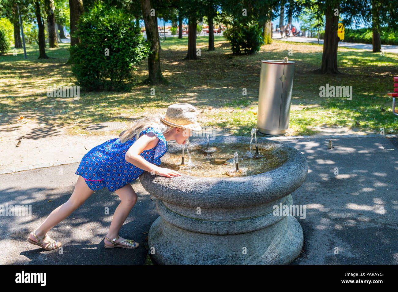 Child, girl kid, drinking from a public fresh water fountain, park on a hot sunny day Stock Photo
