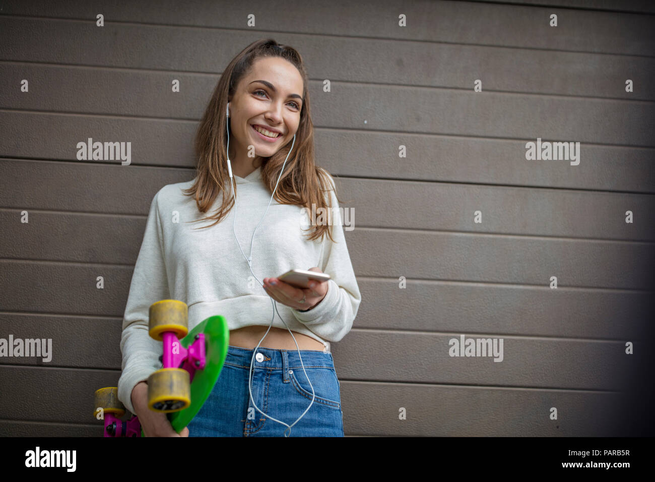 Smiling teenage girl with cell phone, earphones and skateboard Stock Photo