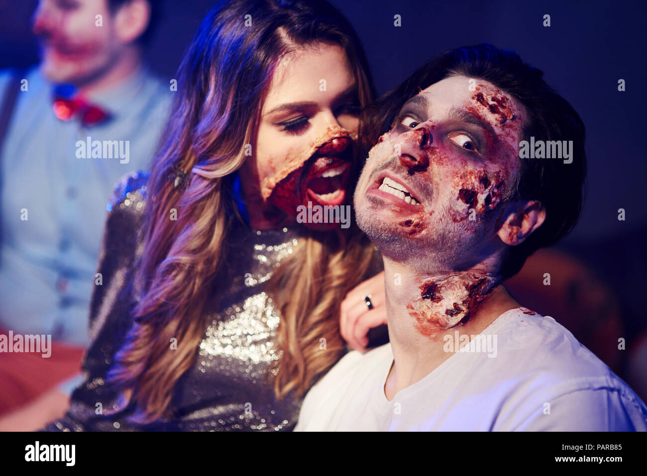 Creepy woman trying to bite her boyfriend at Halloween party Stock Photo