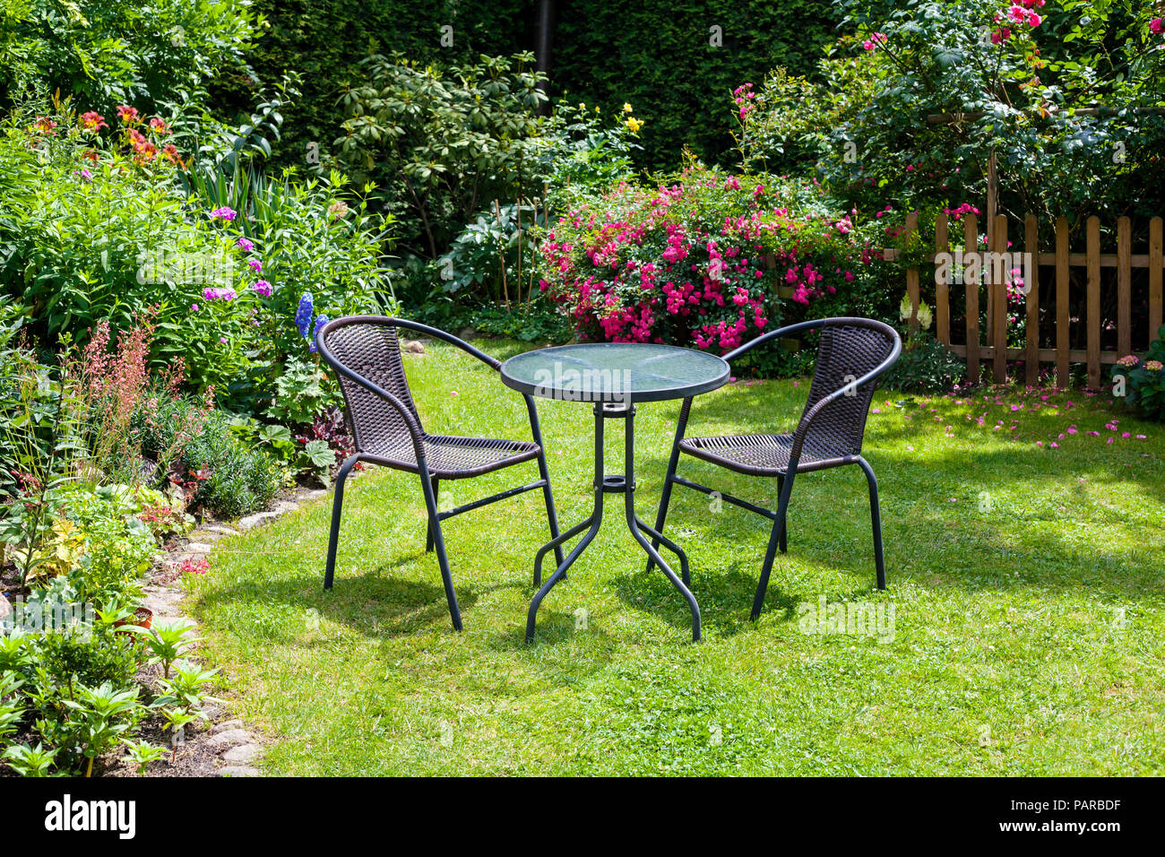 Table and chairs in the garden full of summer flowers Stock Photo