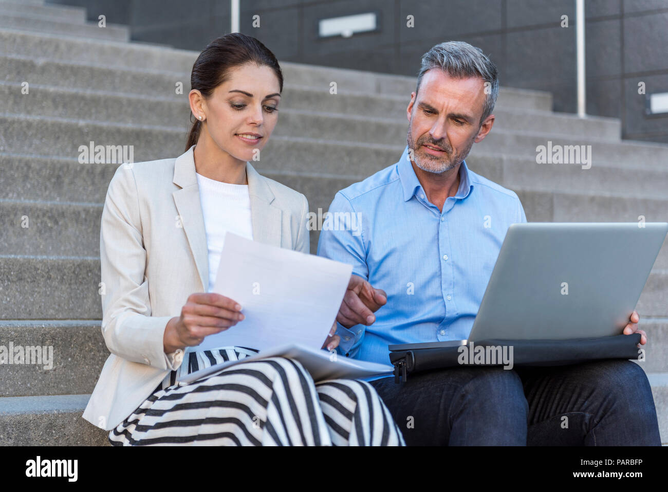 Two business people sitting side by side on stairs working together Stock Photo