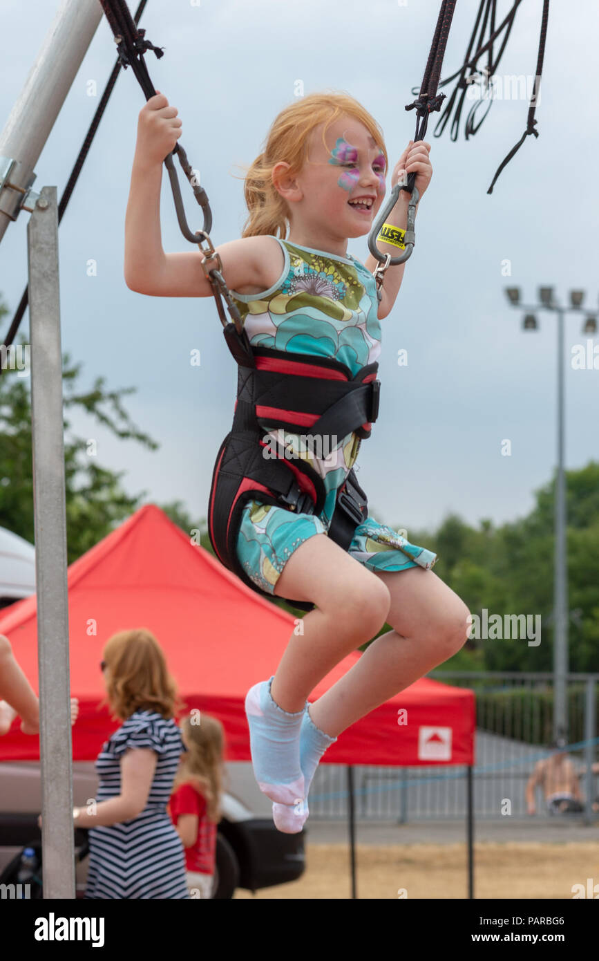 Young girl with red hair smiling and wearing face paints on a bungee trampoline at a family festival in summer. Stock Photo