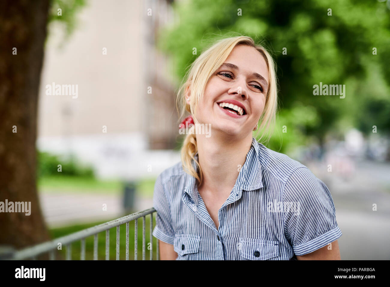 Laughing blond young woman at a fence Stock Photo