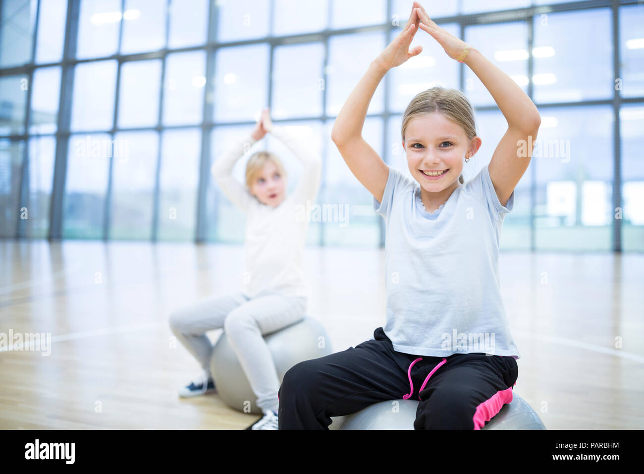 Portrait of smiling schoolgirls sitting on gym balls in gym class Stock Photo