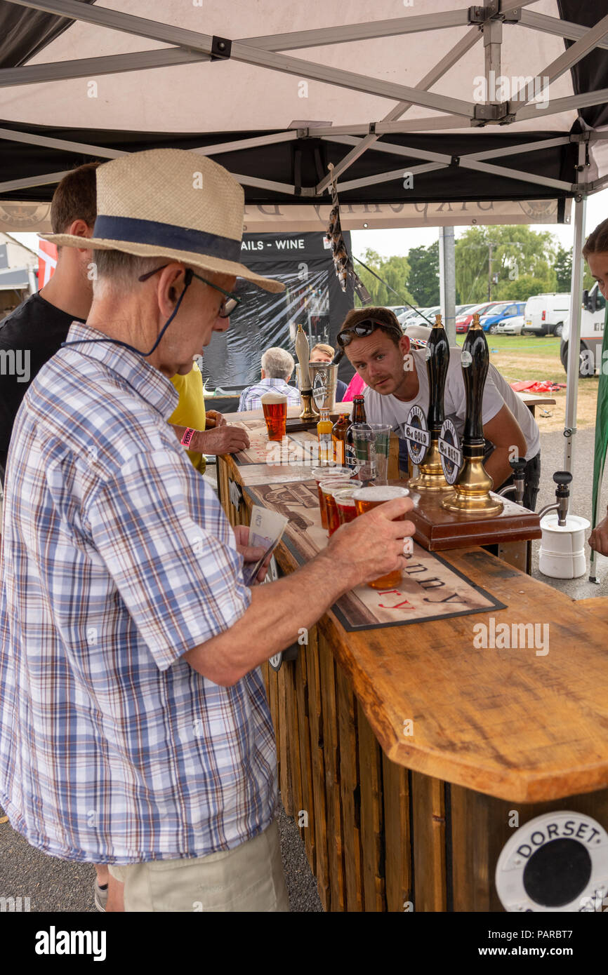 Elderly, mature man wearing a hat and buying beer at an outdoor festival in summer in the UK. Stock Photo
