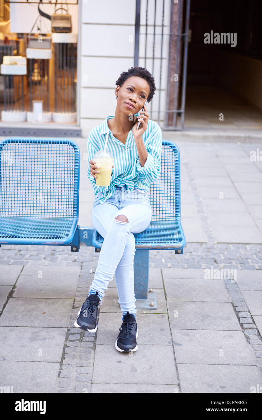 Portrait of woman on the phone sitting in the city with smoothie Stock Photo