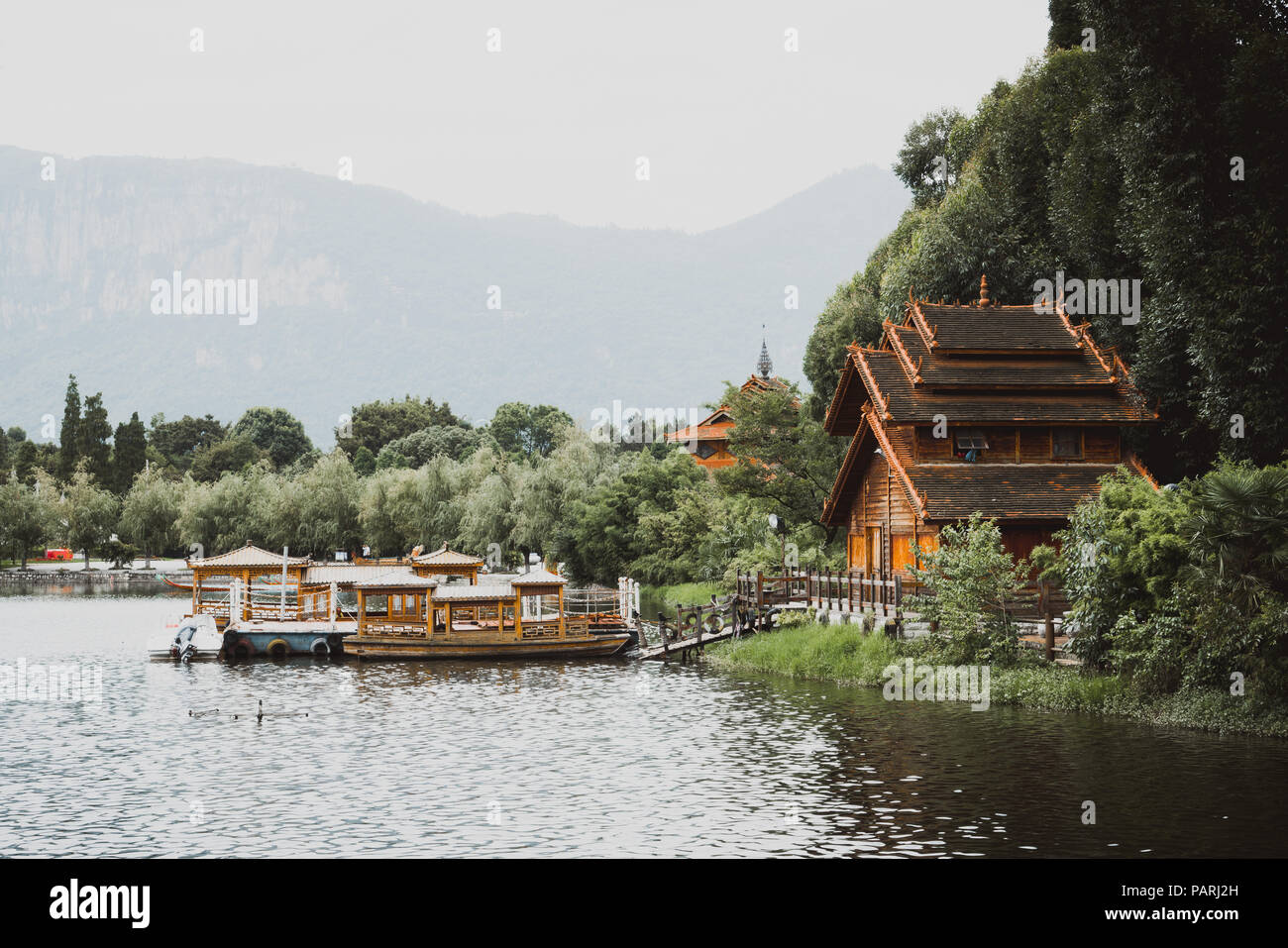 Traditionally built house by a lake and boats in Yunnan Nationalities Village in Kunming, China Stock Photo
