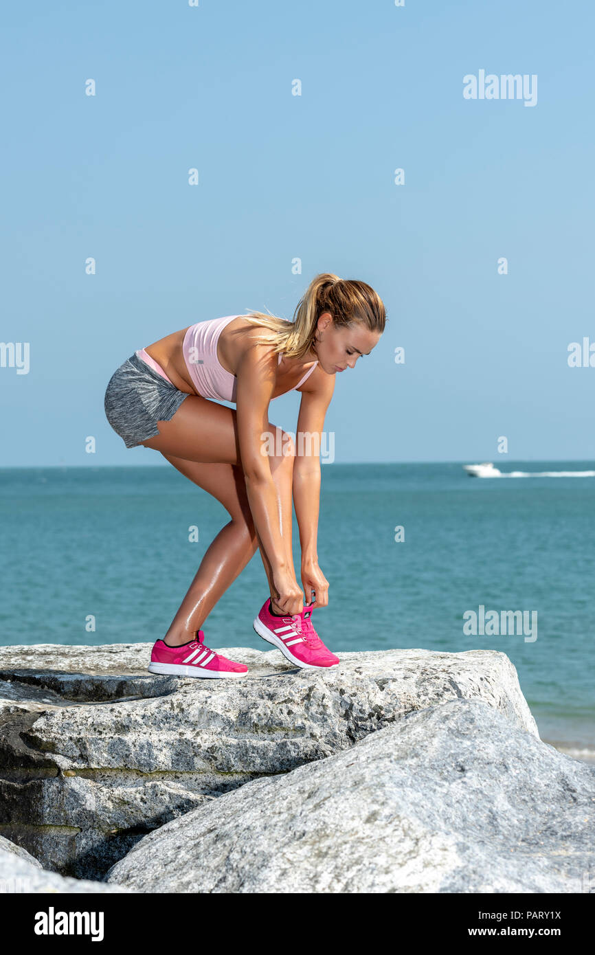woman jogger doing up her trainers before running by the sea. Stock Photo