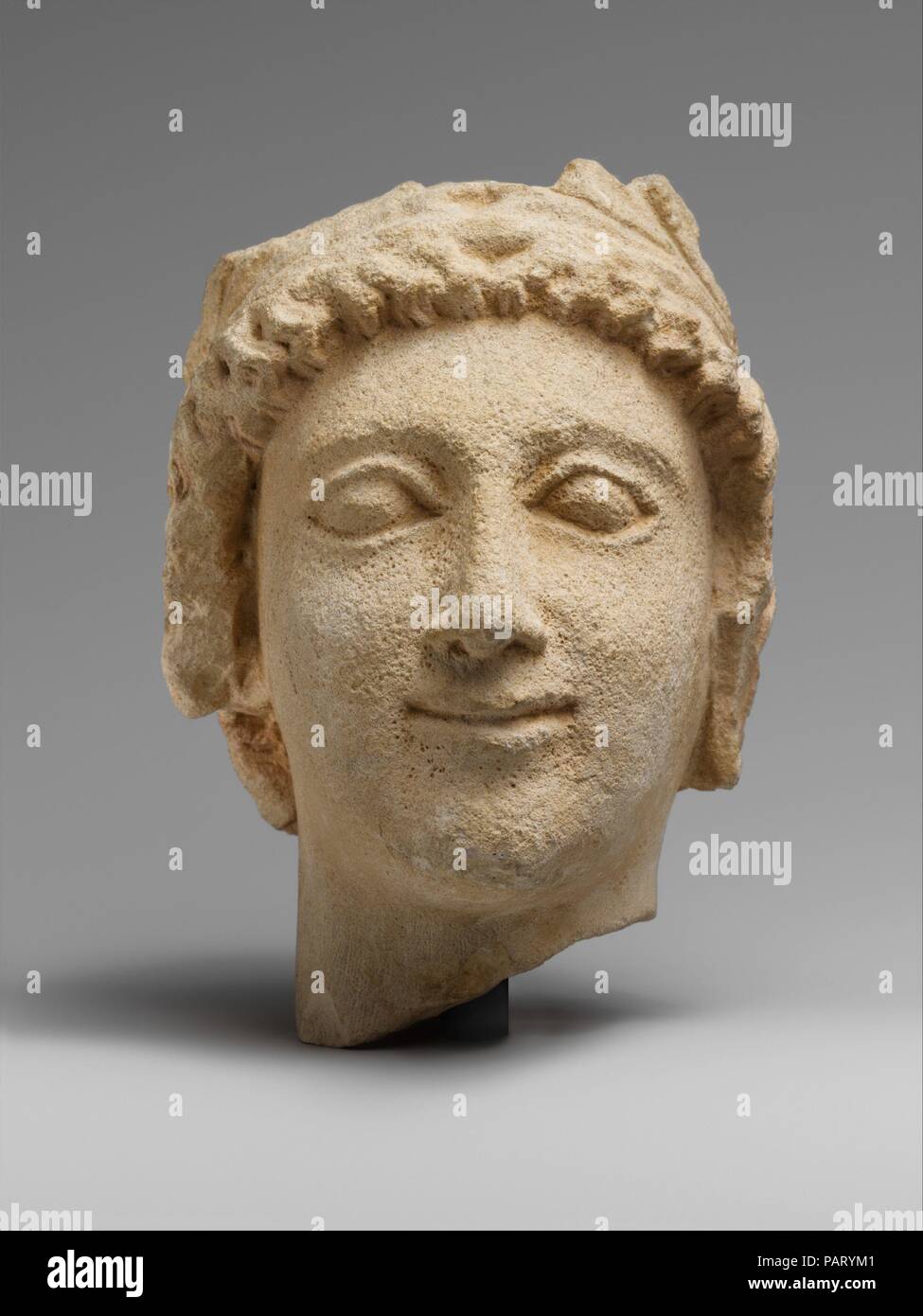 Limestone head of a wreathed youth. Culture: Cypriot. Dimensions: Overall: 5 1/2 x 3 3/8 x 4 3/4 in. (14 x 8.6 x 12.1 cm). Date: 5th century B.C..  Head of a youth wearing a wreath with an oval-shaped, smiling face, a long pointed nose, bulging eyeballs with thick eyelids, and low-set eyebrows. Museum: Metropolitan Museum of Art, New York, USA. Stock Photo