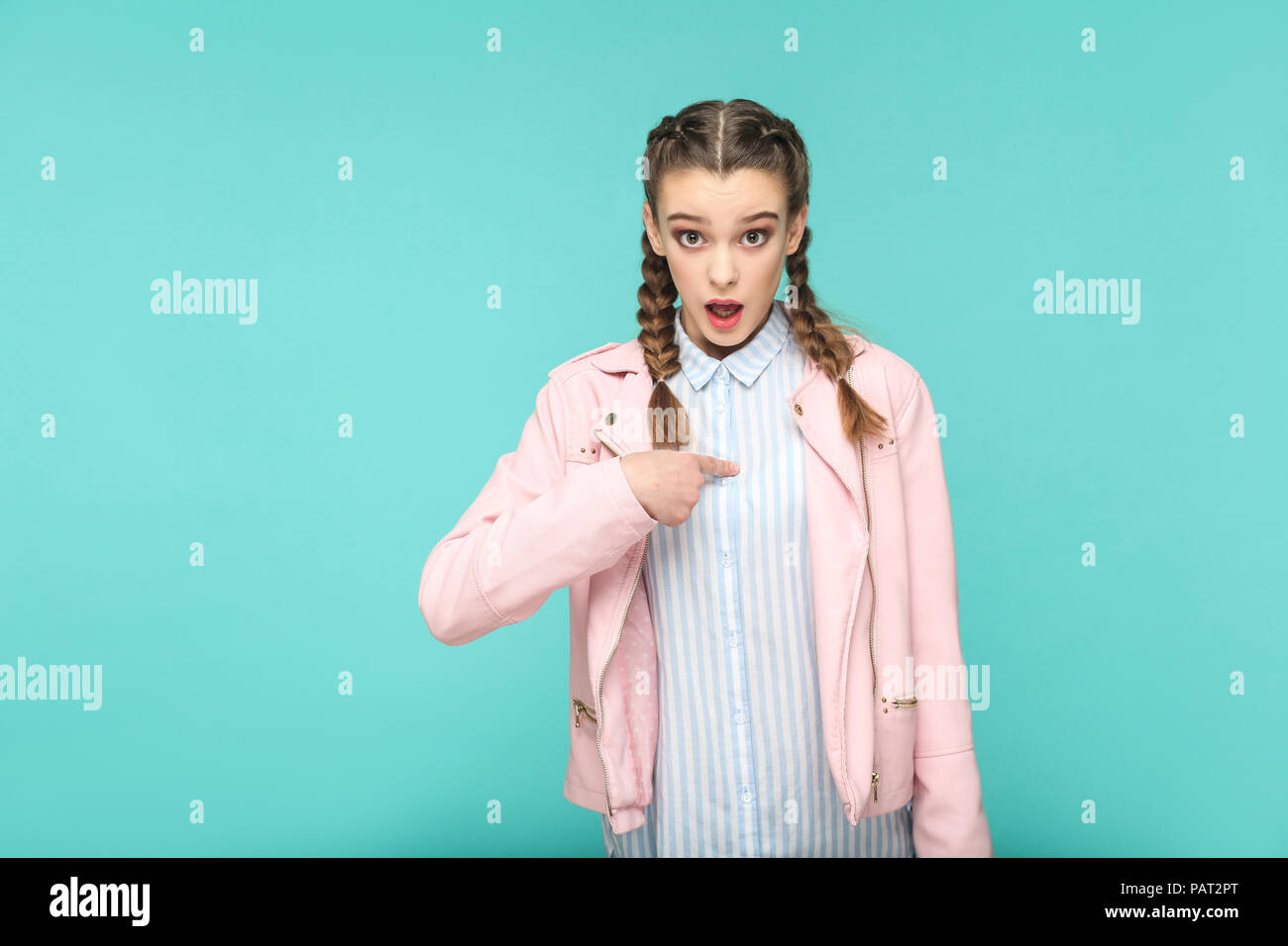 is it me? shocked portrait of beautiful cute girl standing with makeup and brown pigtail hairstyle in striped light blue shirt pink jacket. indoor, st Stock Photo