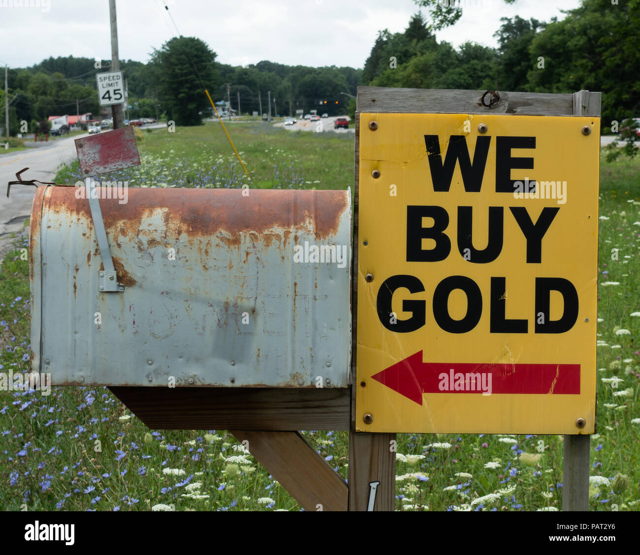 A beat up bright yellow We Buy Gold sign with a red arrow next to a rusty old mail box on a side road in upstate NY, USA Stock Photo