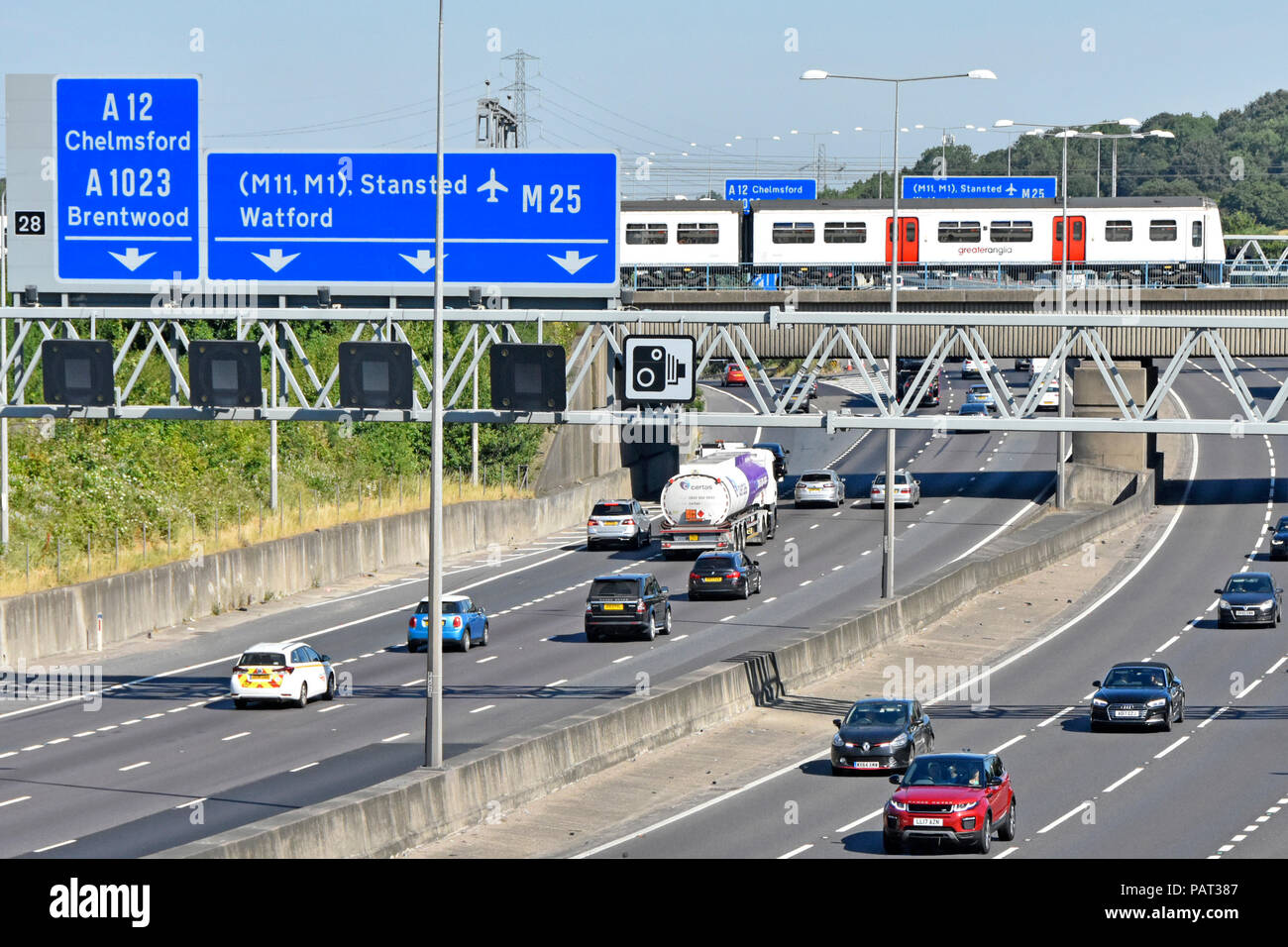View from above looking down on traffic M25 motorway gantry road sign junction 28 Brentwood Essex Greater Anglia train on railway bridge England UK Stock Photo