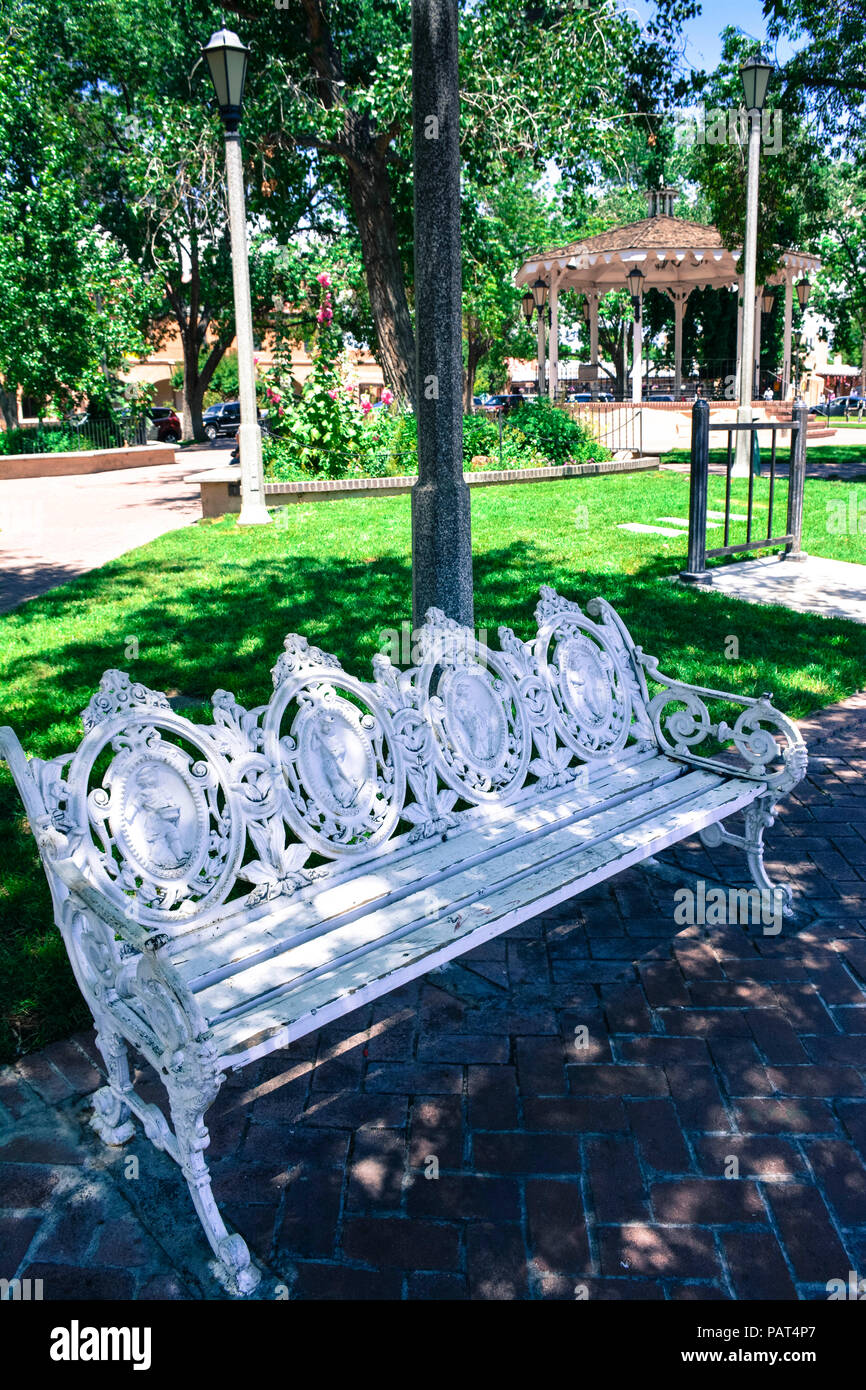 An old fashioned ornate iron scroll work park bench with wooden seat in plaza near gazebo in old town Albuquerque NM Stock Photo