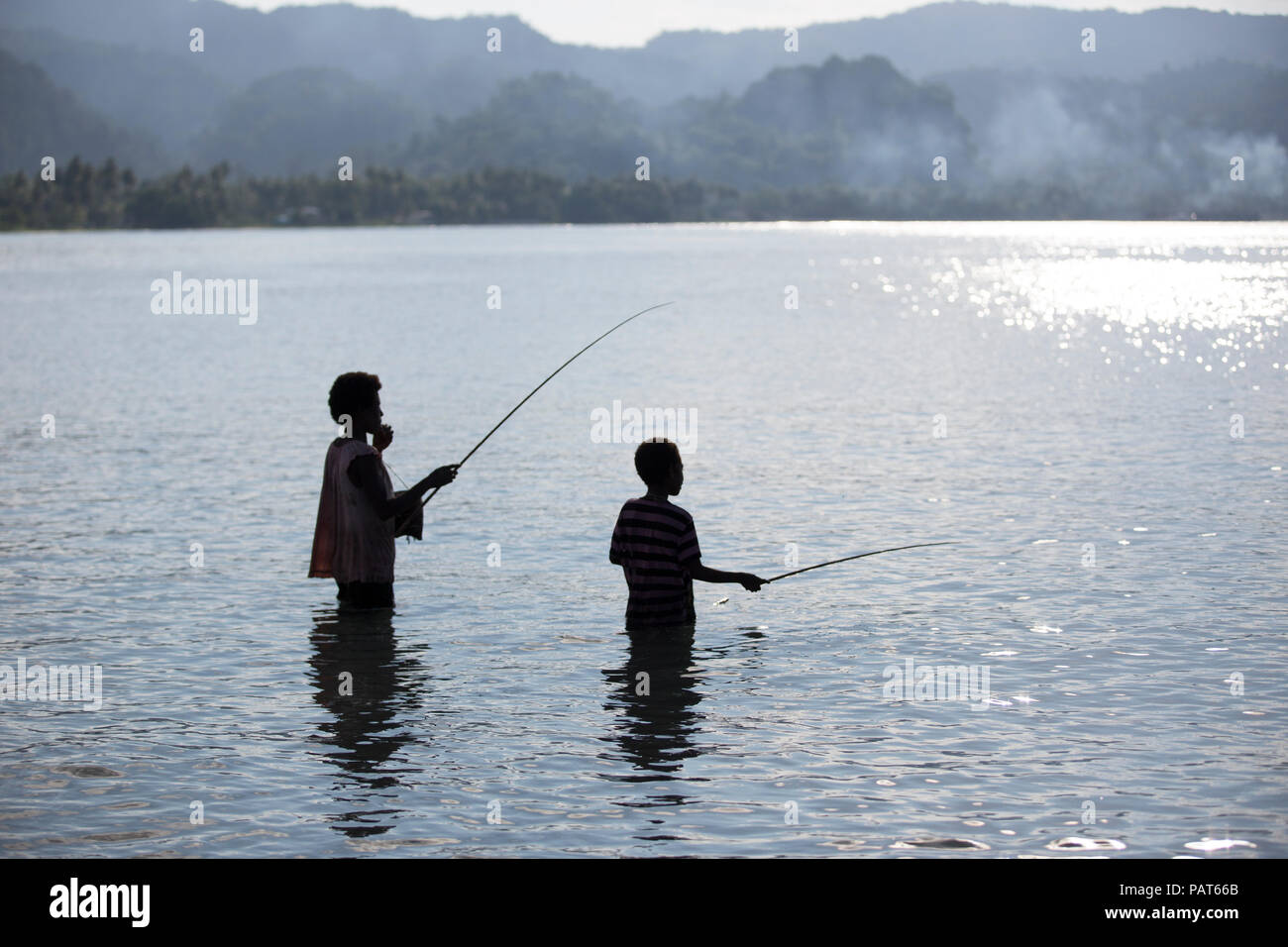 Papua New Guinea, Vanimo, silhouette of mother and child fishing in water. Stock Photo