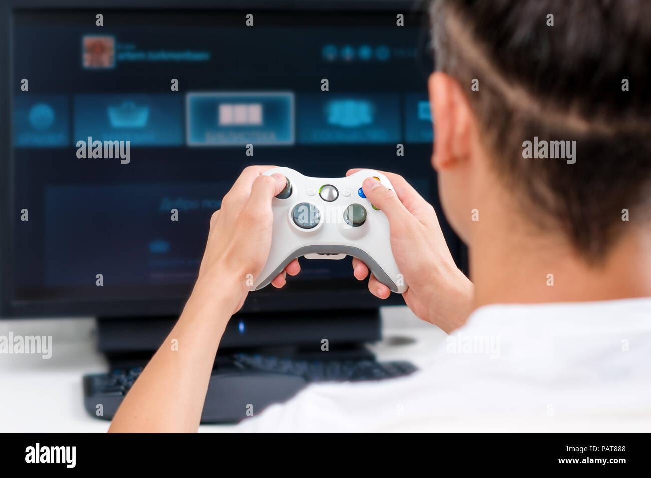 Happy young man playing and winning online game on computer. Back view of  gamer with video console gamepad controller. Competitive gaming, electronic  sports, technology, gaming, entertainment concept. Stock Photo