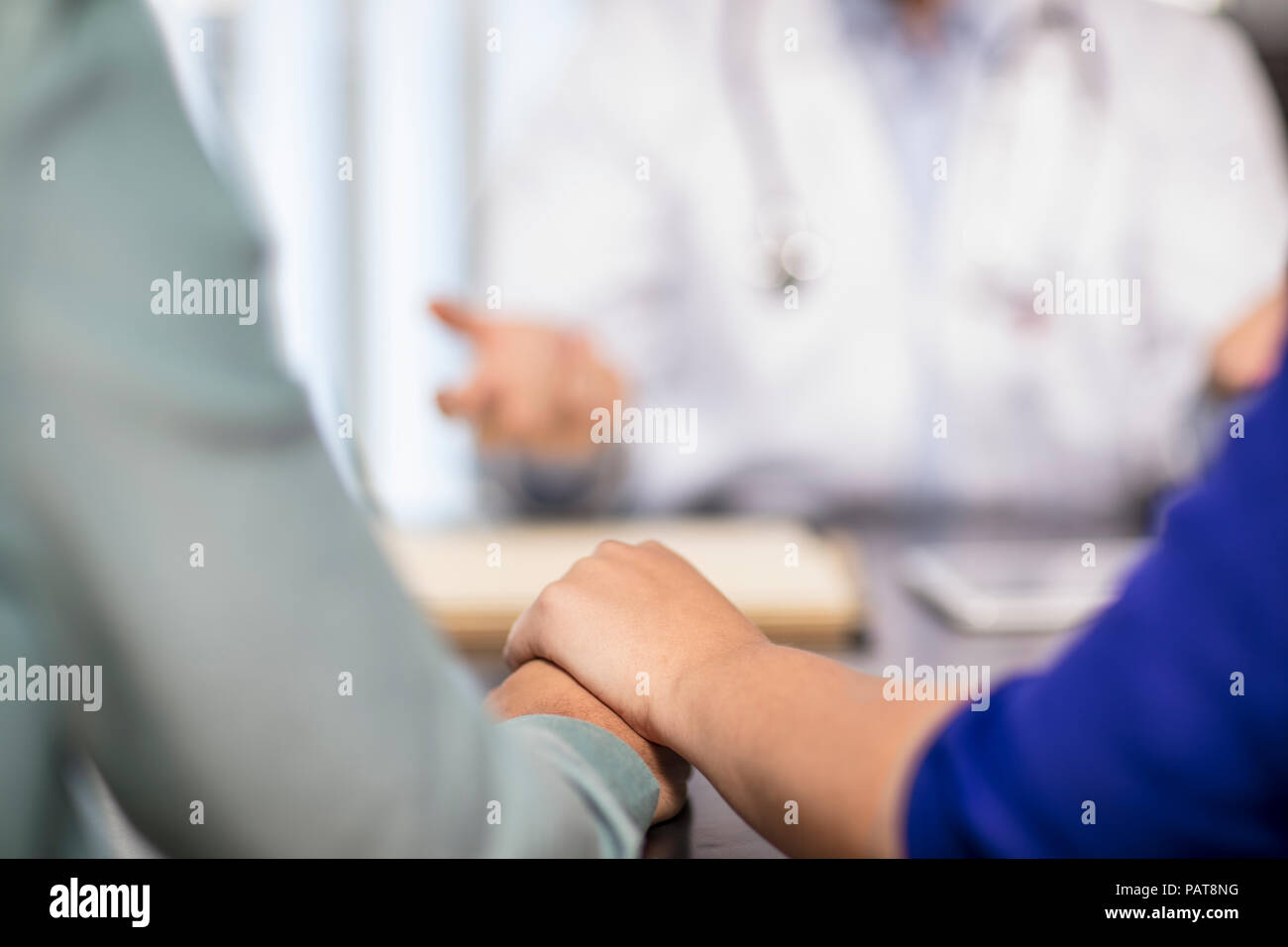 Doctor and couple holding hands in medical practice Stock Photo
