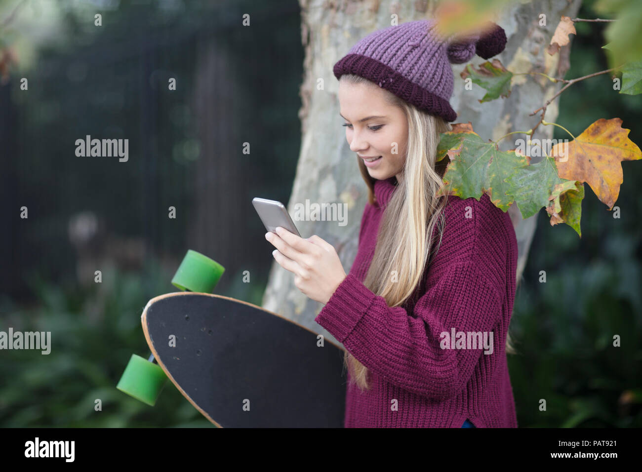 Smiling teenage girl looking at cell phone holding skateboard Stock Photo