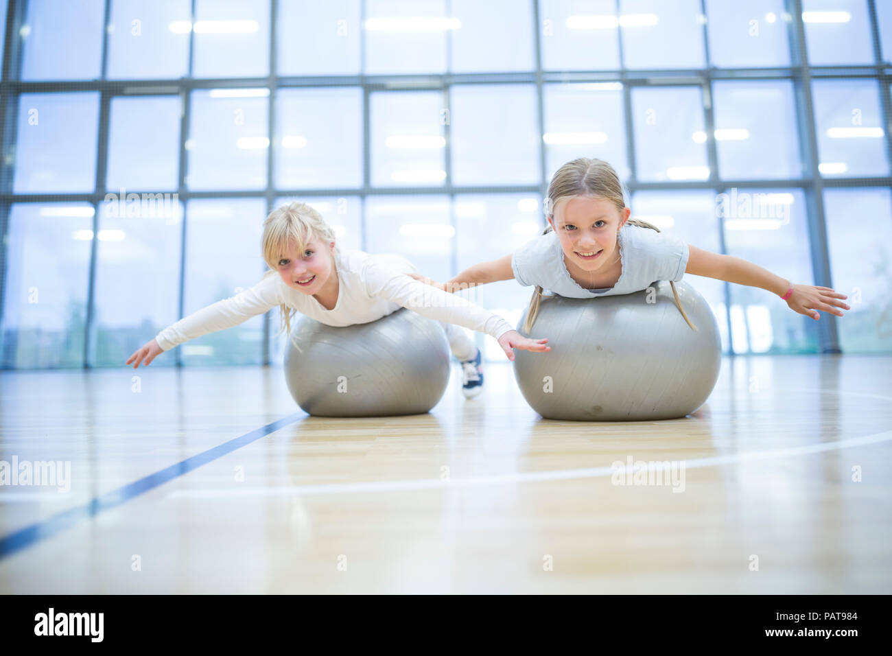 Portrait of smiling schoolgirls balancing on gym balls in gym class Stock Photo