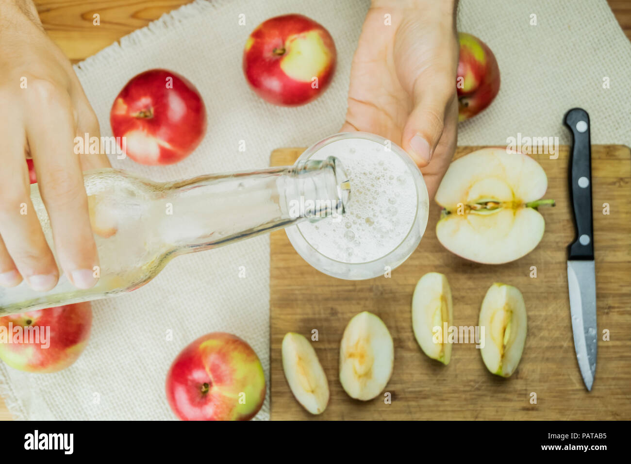Pouring sparkling apple cidre drink into glass, top view. Flat lay image with hands fixing a drink of cider on rustic wooden table background with rip Stock Photo