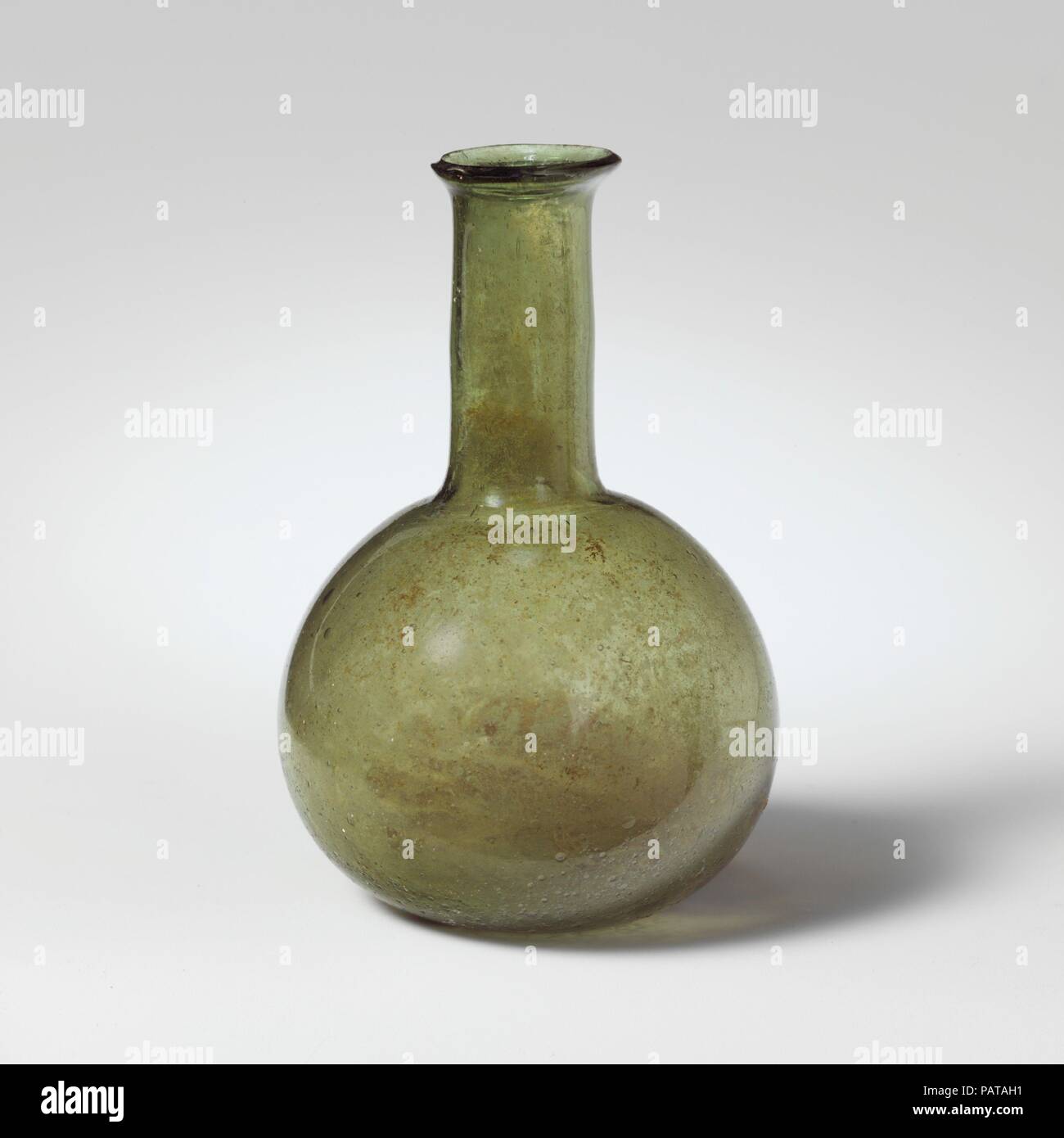Glass perfume bottle. Culture: Roman. Dimensions: 3 3/16 in. (8.1 cm)  Diameter: 2 1/16 x 13/16 in. (5.2 x 2.1 cm). Date: 3rd century A.D. or later.  Translucent green.  Rim folded out with beveled lip; tall cylindrical neck; globular body; flattened bottom with large circular pontil mark.  Intact; many pinprick and larger bubbles; faint iridescence on exterior; patches of weathering and soil encrustation on interior. Museum: Metropolitan Museum of Art, New York, USA. Stock Photo