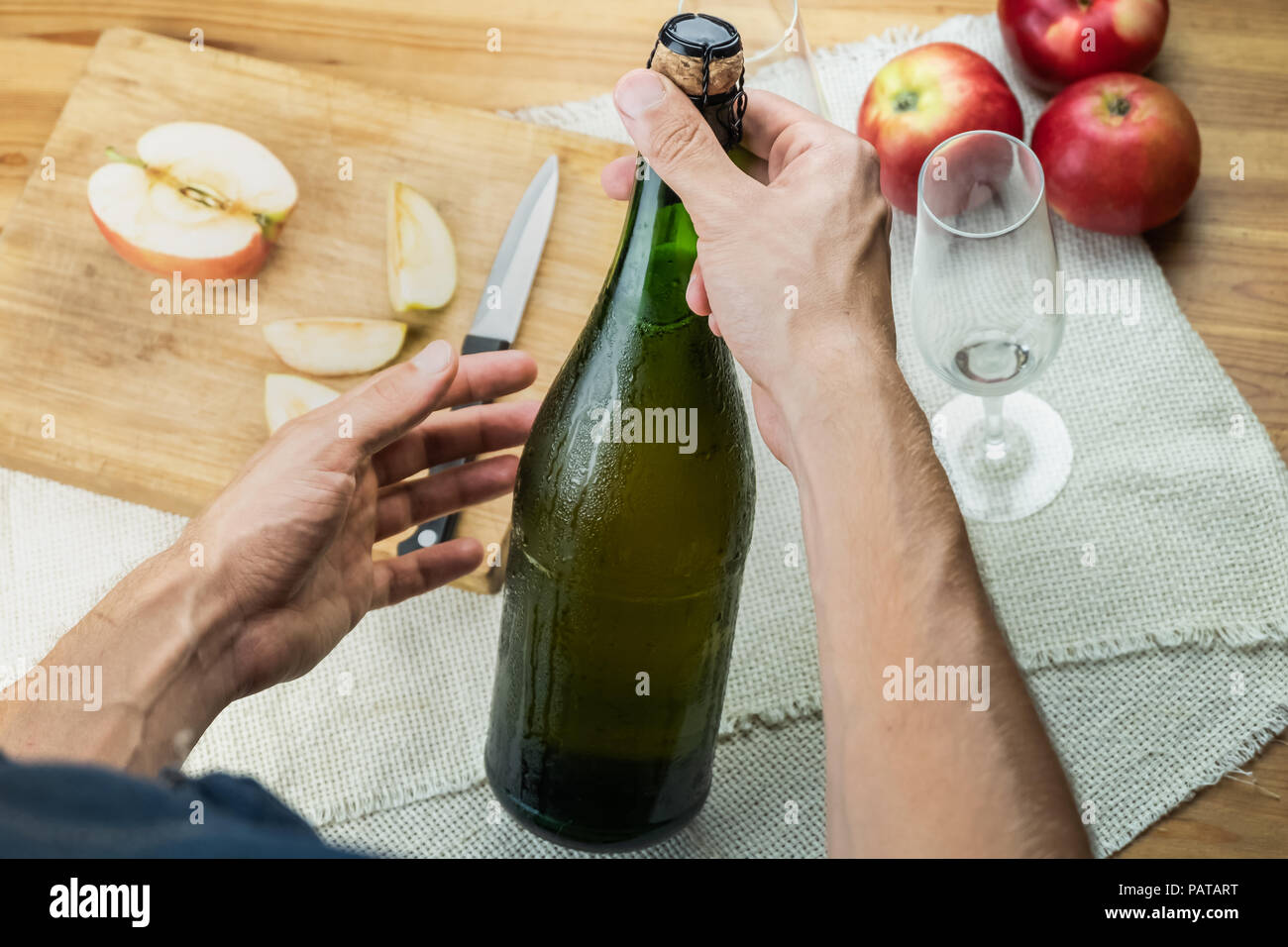Top view of male hands holding corked bottle of premium cidre. Shot from above with beautiful ice cold bottle of apple wine in man's hands, with local Stock Photo