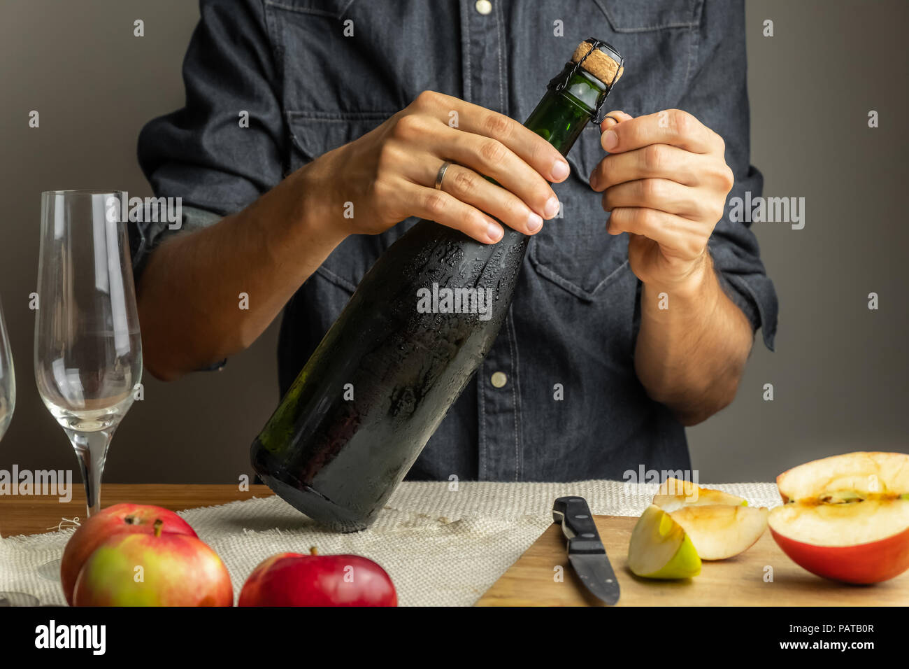 Male hands opening bottle of premium cidre. Uncorking beautiful ice cold bottle of apple wine, with ripe apples in background Stock Photo