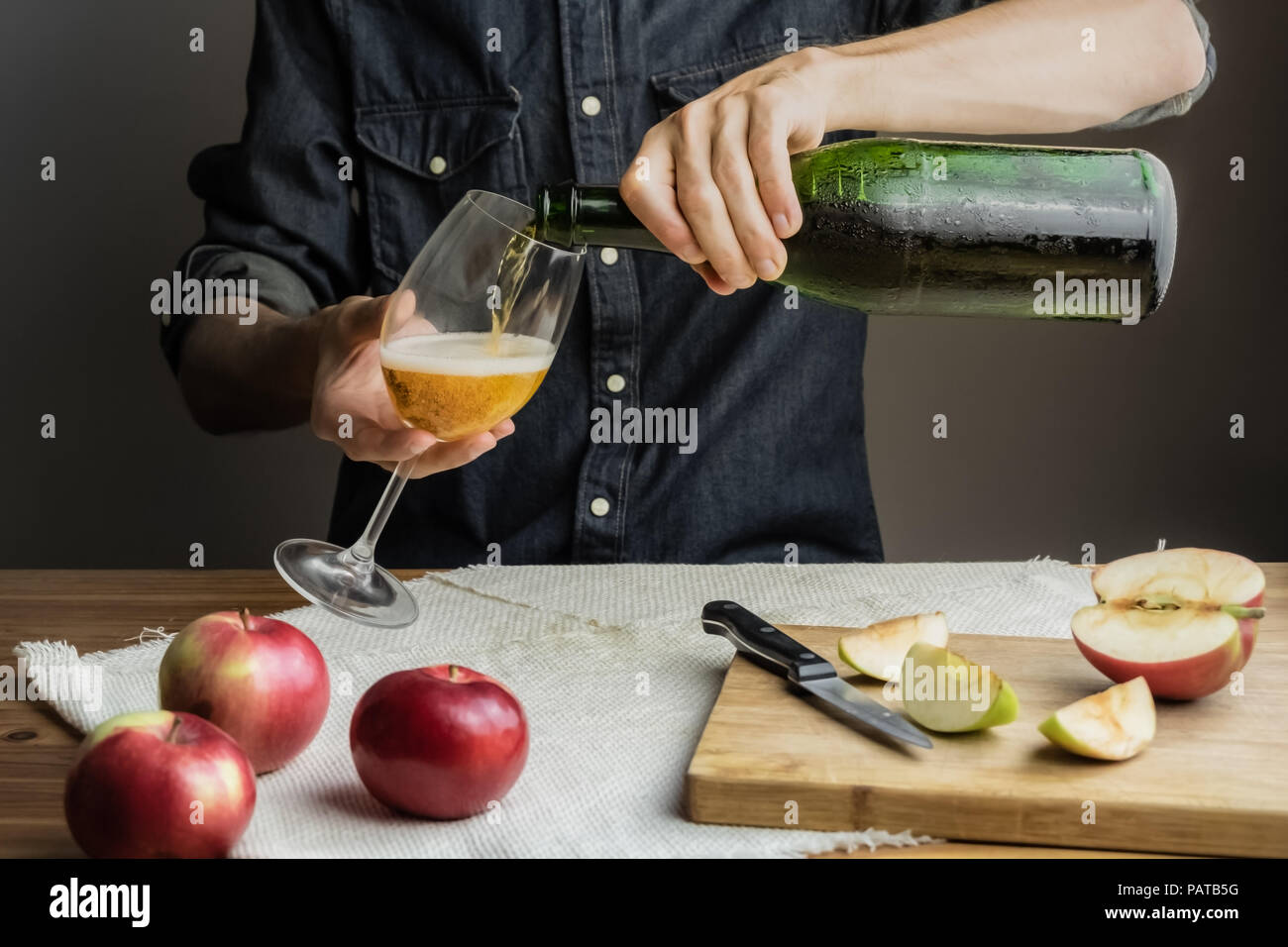 Male hands pouring premium cidre in wine glass above rustic wood table. Man pours a glass of vintage apple wine out of ice cold bottle Stock Photo