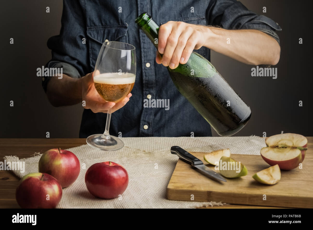 Male hands pouring premium cidre in wine glass above rustic wood table. Tasting vintage apple cider out of ice cold bottle Stock Photo