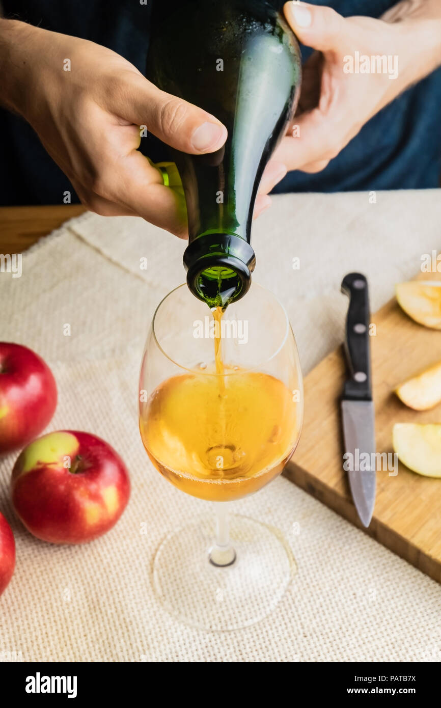 Top view of man pouring premium cidre in glass. Close-up of male hands pouring vintage apple wine into beautiful glass in rustic table background with Stock Photo