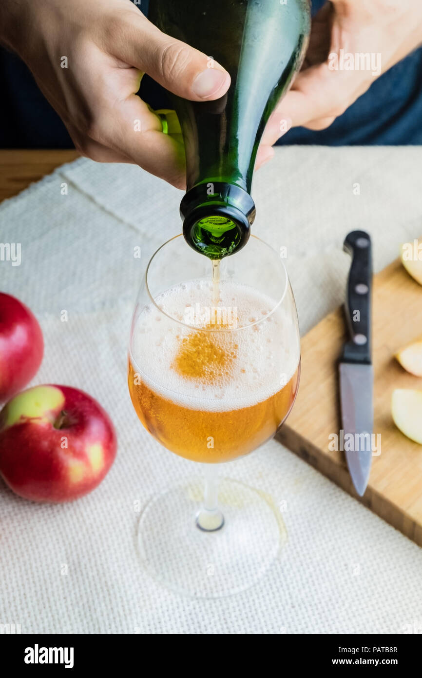 Close-up image of man pouring premium cidre in glass. Top view of male hands pouring vintage apple wine into beautiful glass in rustic table backgroun Stock Photo