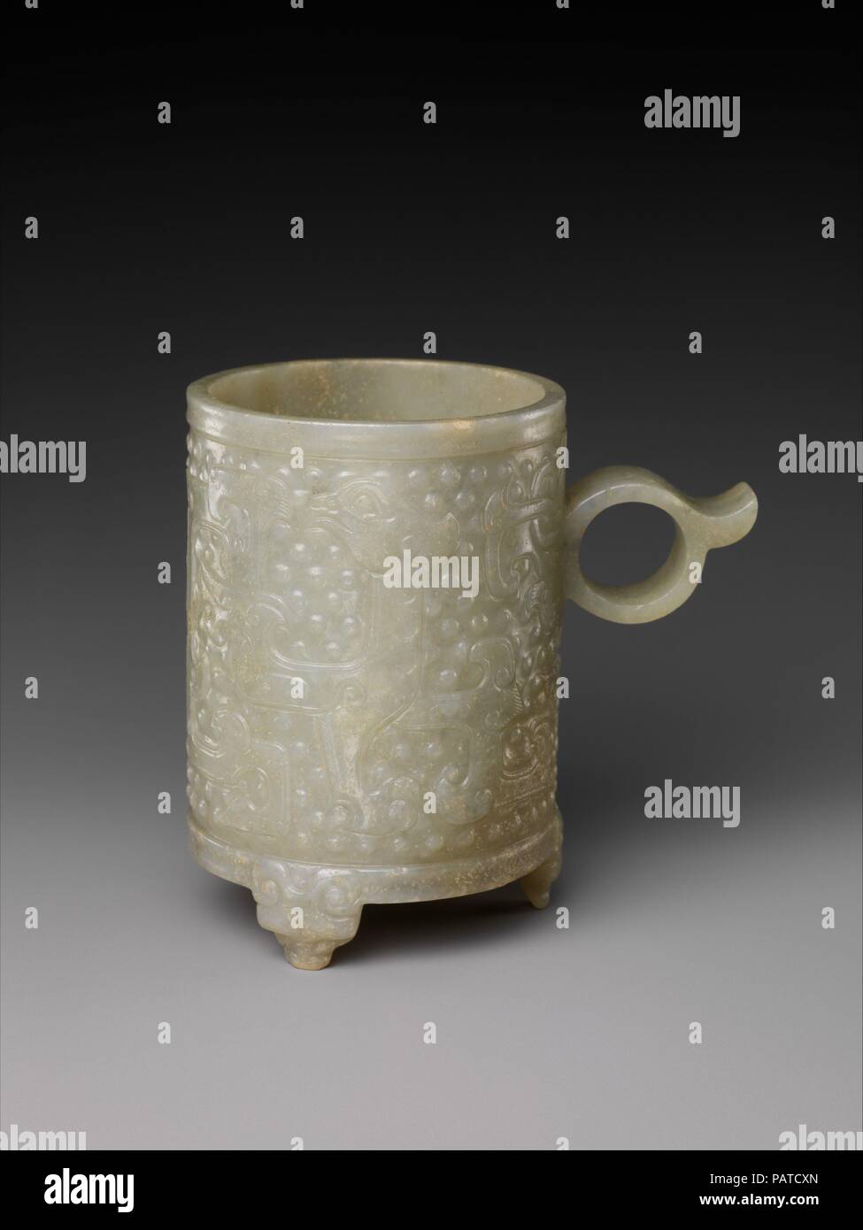 Cup with ring handle and archaic designs. Culture: China. Dimensions: H. 3 3/4 in. (9.5 cm). Date: 16th-17th century.  The abstract bodies of the two intertwined birds on the surface of this cup can be traced to the Bronze Age. The shape of the cup is based on similar jade cups of the Western Han dynasty (206 B.C.-A.D. 9), and so are the multiple raised dots in the background, which derive ultimately from the simulated granulation on the surface of metalwork of the late Eastern Zhou dynasty (770-256 B.C.). Museum: Metropolitan Museum of Art, New York, USA. Stock Photo