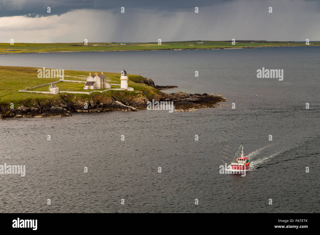 Lighthouse on the coast of Orkney, Scotland with a passing boat Stock Photo