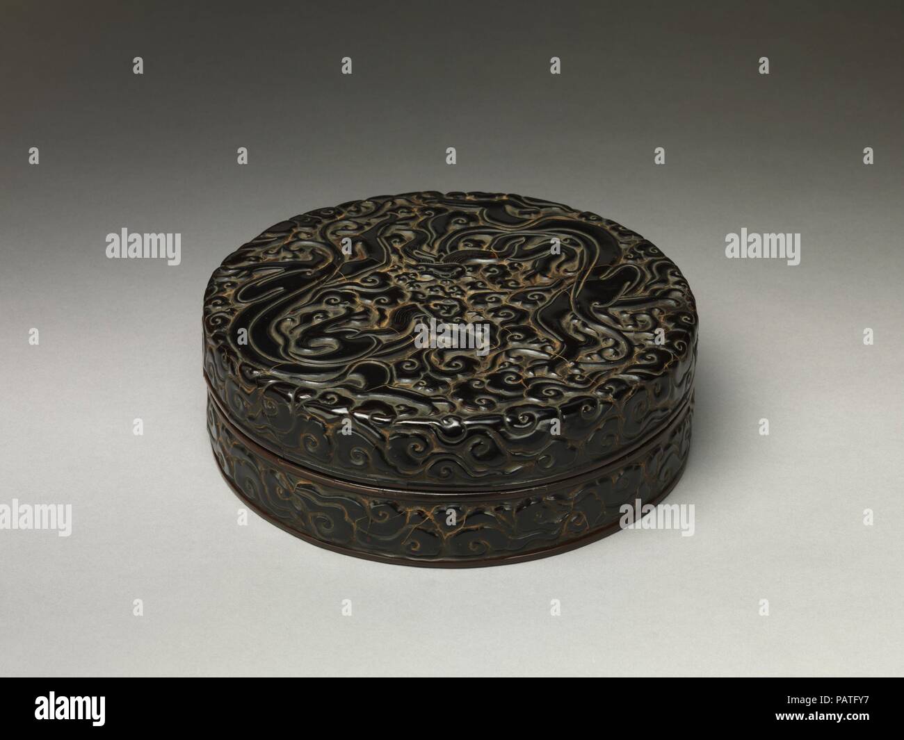 Box with chi dragons amid clouds. Culture: China. Dimensions: H. 3 in (7.6 cm); Diam. 9 5/8 in. (24.4 cm). Date: 13th century.  Known as chi, the feline dragons that curve along the surface of this box were inspired by comparable creatures found on Bronze Age vessels, which were rediscovered during the Song dynasty and often reinterpreted in the arts of that period. Although they lack the large horns, prominent snouts, and scaled body of the typical Chinese depiction of the dragon, chi dragons are also regarded as auspicious and protective. Museum: Metropolitan Museum of Art, New York, USA. Stock Photo