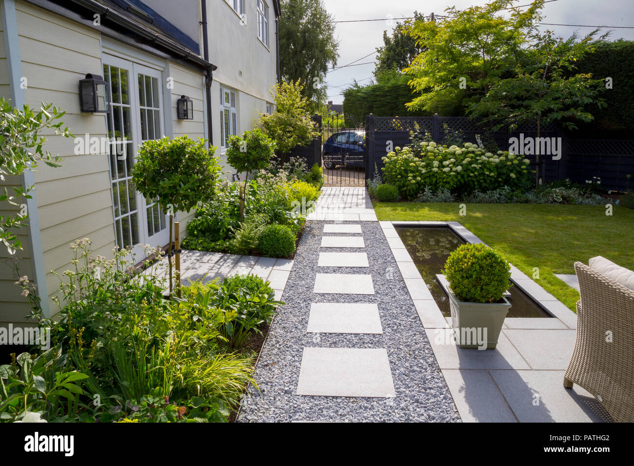 View along London Stone granite paving towards gated entrance, with herbaceous borders, pool water feature and Viburnum tinus topiary Stock Photo