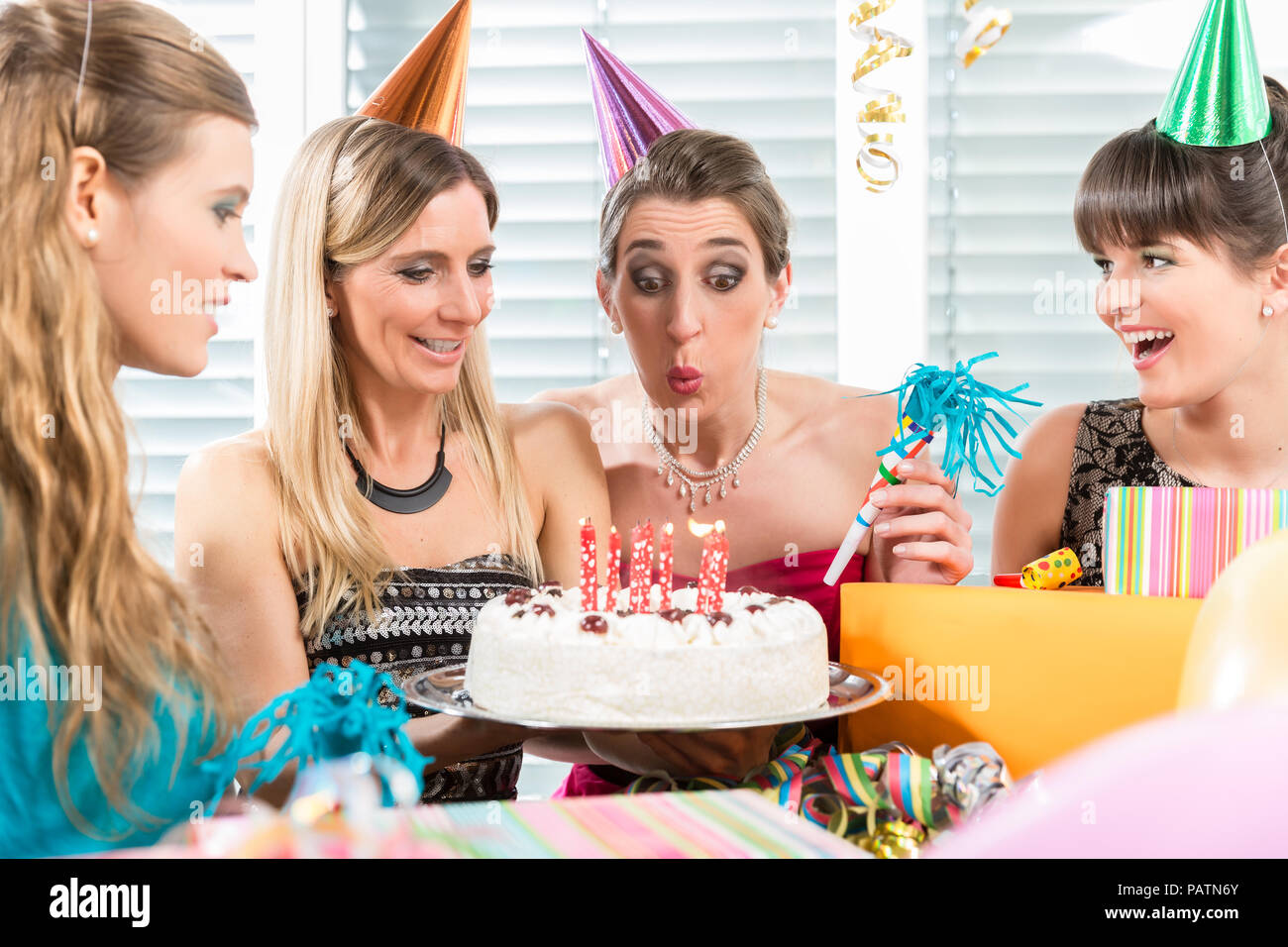 Woman blowing out candles on her birthday cake while celebrating Stock Photo