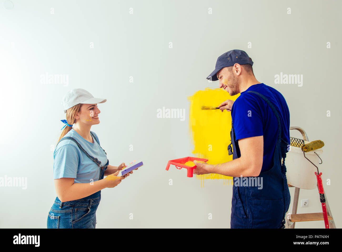 Couple decorating room using paint rollers and paintbrush on wall Stock Photo