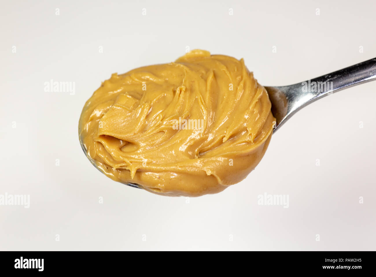 A swirl of peanut butter on a spoon about to be spread onto a bread