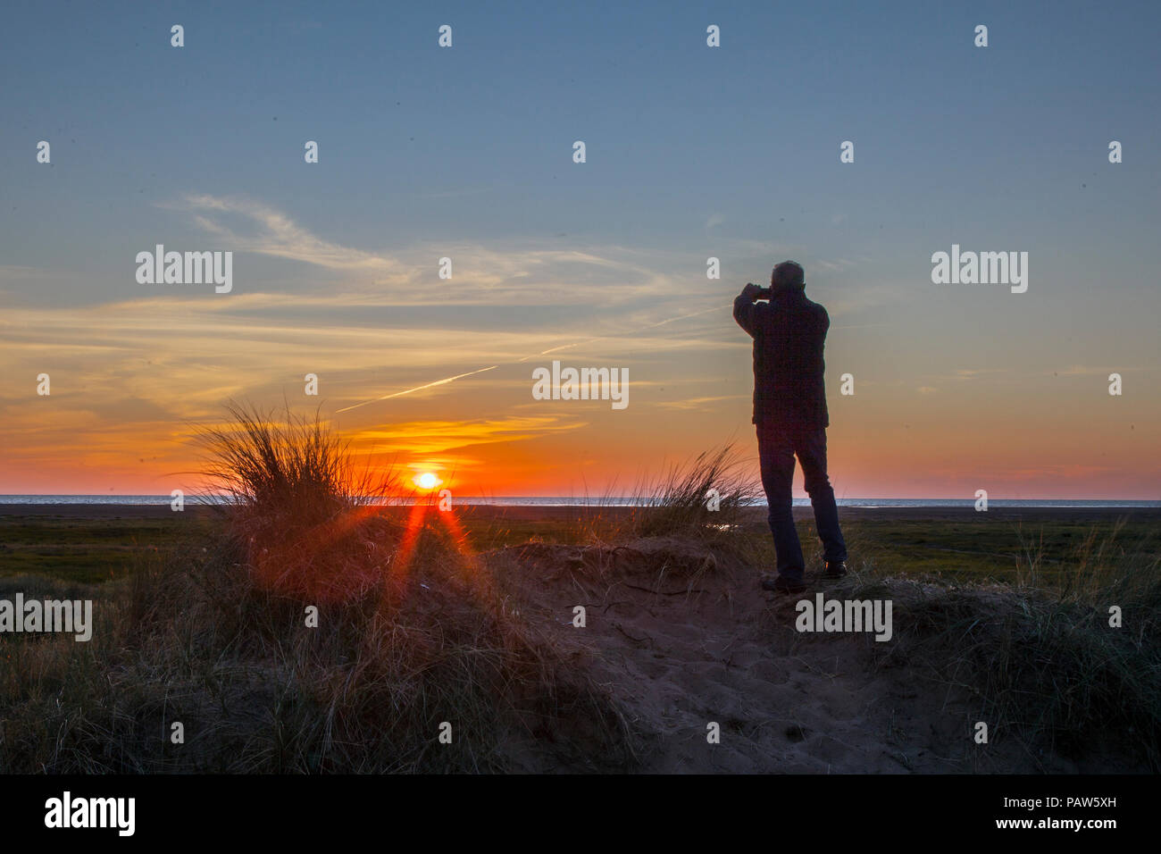 Southport, Merseyside, UK 14th July, 2018. Silhouette man. UK Weather. Colourful sunset over the Irish Sea and Ainsdale Sand Dunes National Nature Reserve (NNR), which is a 508-hectare site comprising rare dunes, beach and woodland habitats. There are 10 kms of way-marked footpaths to follow, a tranquil and wild place surrounded by one of the most urban areas in England. Credit: MediaWorldImages/Alamy Live News Stock Photo